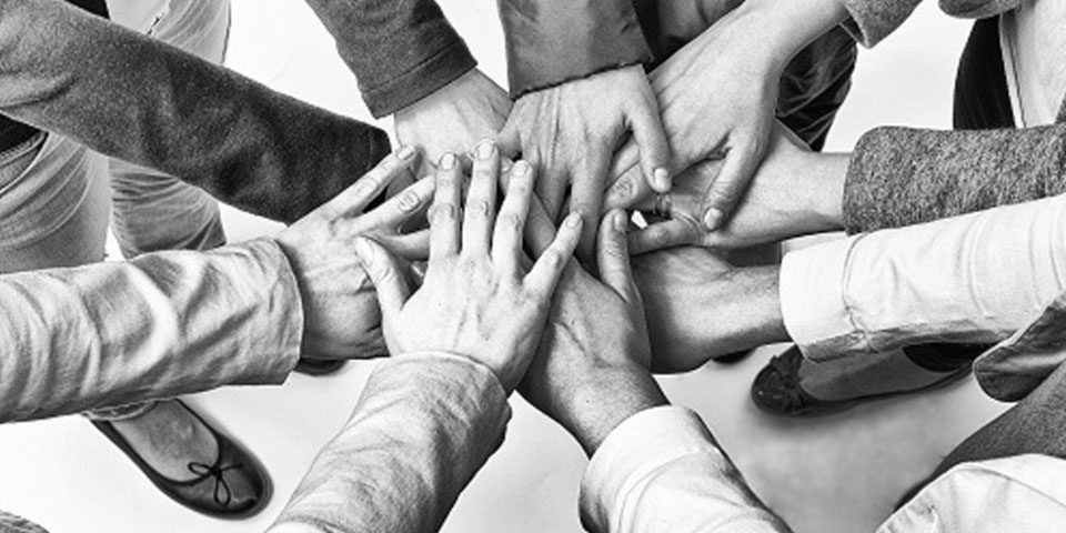 Black and white image of team joining hands in a circle.