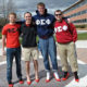 An Image of four gentleman who belong to a fraternity. The men all pose for a picture while wearing bright red heels. The heels represent their contribution to the Walk a Mile in Her Shoes®: The International Men's March. The march is a demonstration to end sexual assault towards women.
