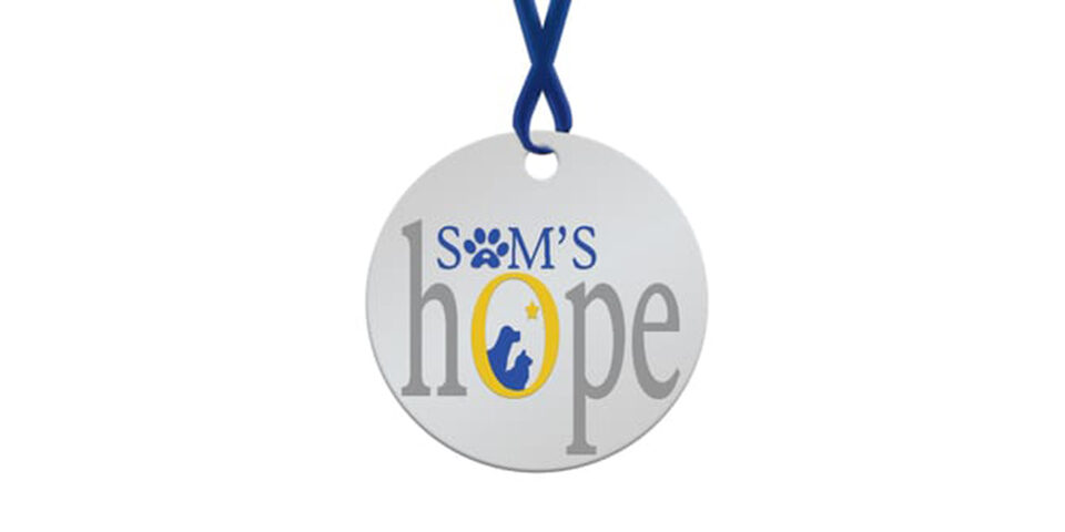 Sams Hope Logo. Shows a round dog tag shape with a blue ribbon looped through a hole towards the top. Sam’s is spelled out in small blue font towards the top. The “A” is a paw print. Hope is in large gray font underneath. The “O” is yellow and contains silhouettes of a dog and cat with a star above them.