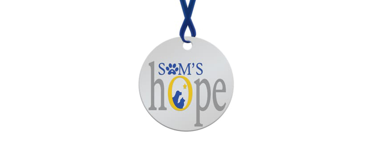 Sams Hope Logo. Shows a round dog tag shape with a blue ribbon looped through a hole towards the top. Sam’s is spelled out in small blue font towards the top. The “A” is a paw print. Hope is in large gray font underneath. The “O” is yellow and contains silhouettes of a dog and cat with a star above them.