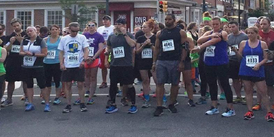 Image of large group of participants in a 5K run. Everyone has a number plate and is prepare for the race to begin.